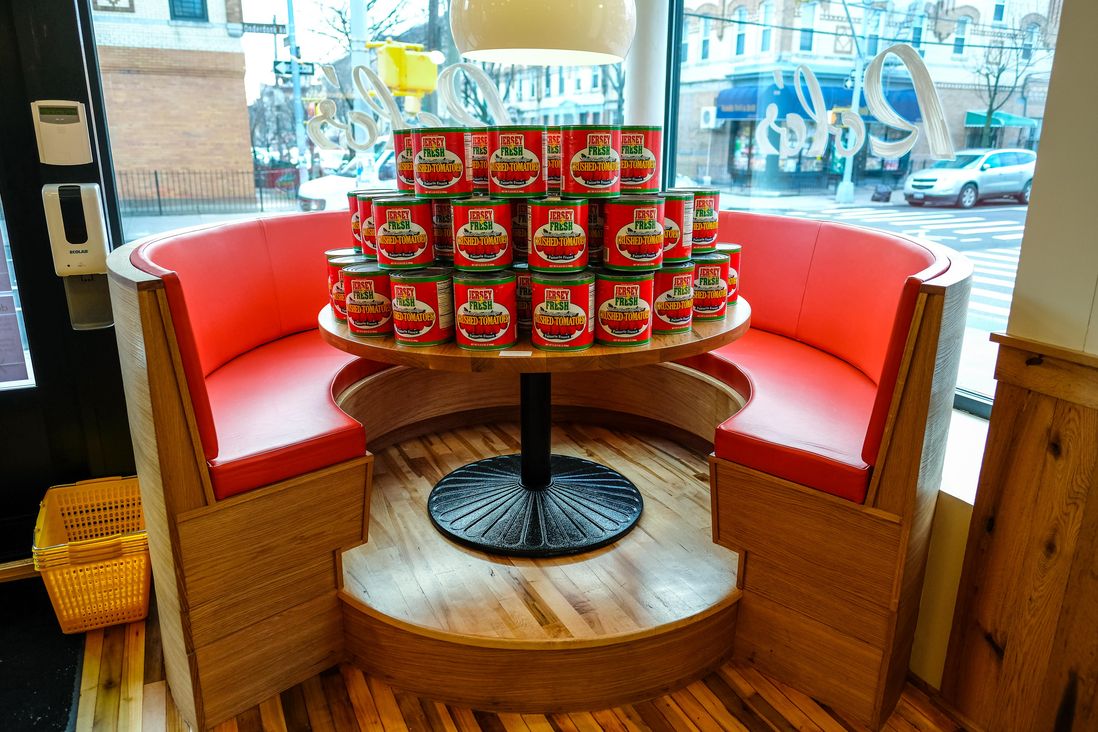 Cans of tomatoes stacked on a table at a red banquette inside Rolo.